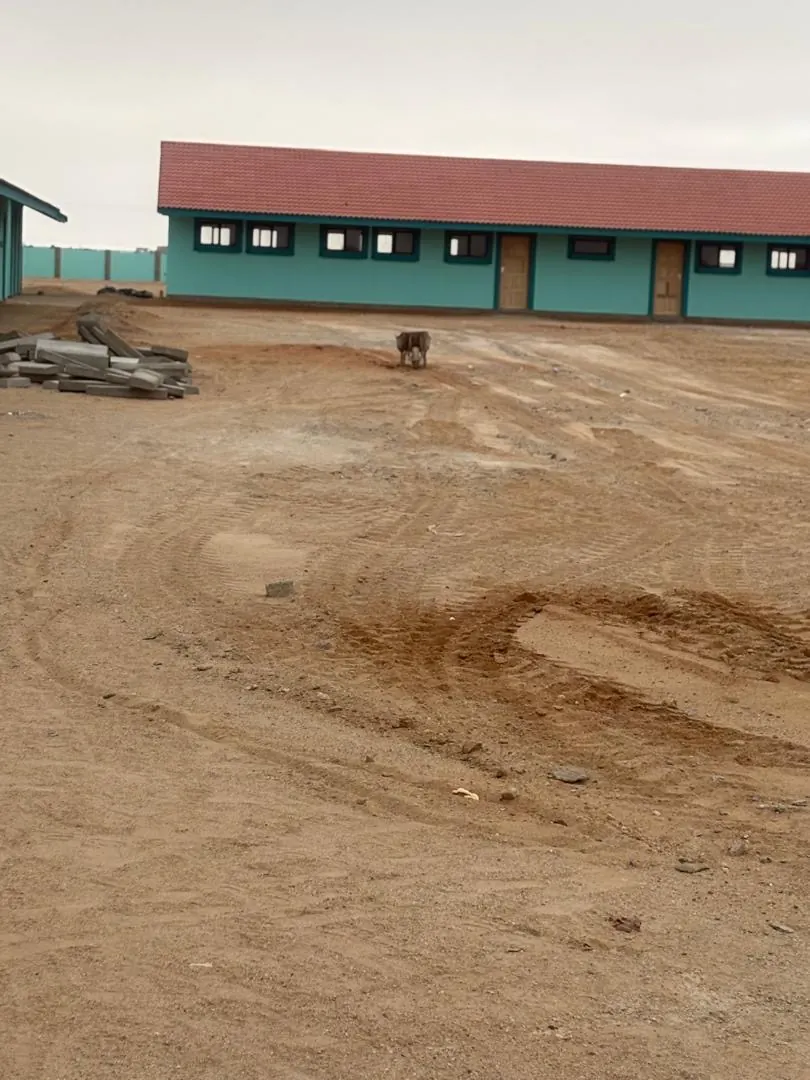 Classroom blocks with red-tiled roofs above the graded yard at the Henties Bay school site